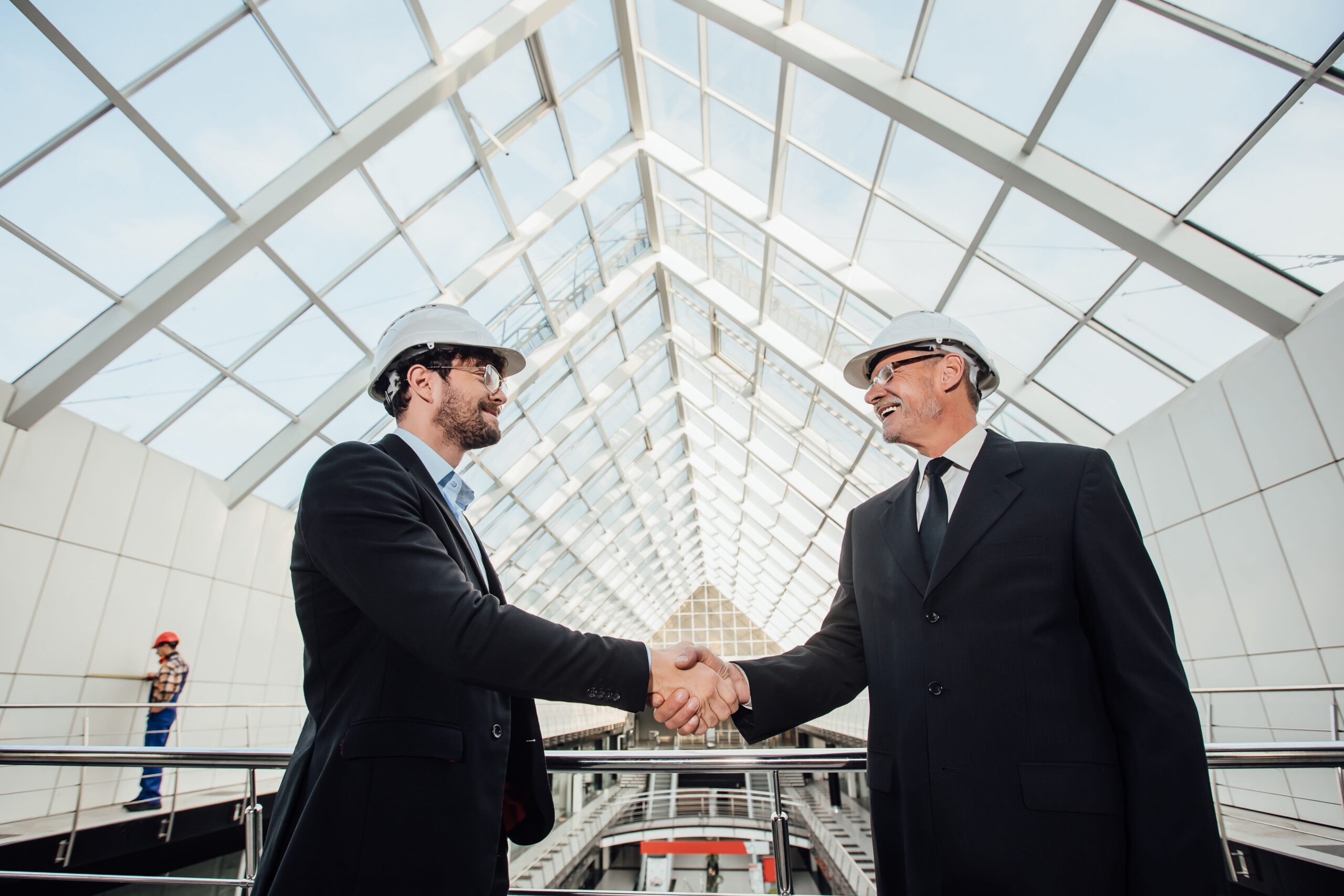 two-cheerful-businessman-handshaking-helmet-new-building-min